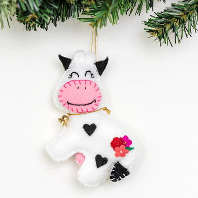 Decorative cow ornament with pink face and black accents hanging on a Christmas tree.