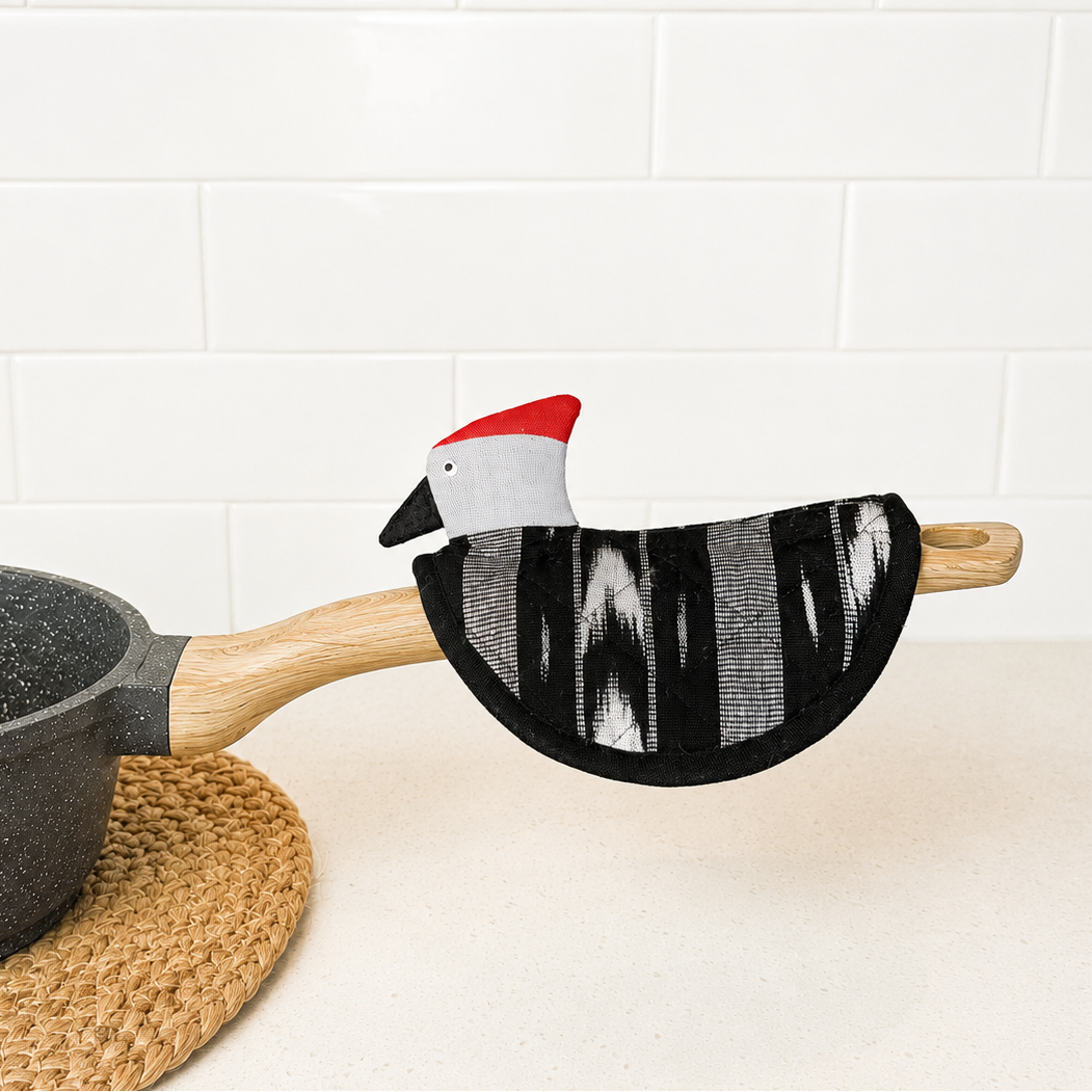 Potholder with a cartoon chicken design on a pot handle against a white tiled wall.