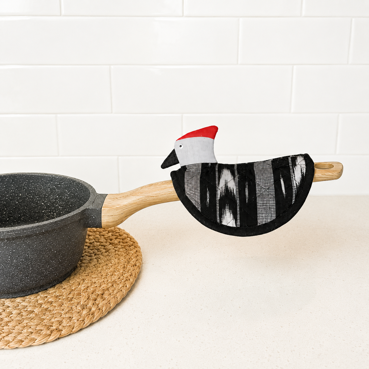 Potholder with a cartoon chicken design on a pot handle against a white tiled wall.